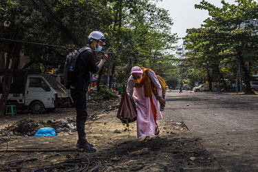 An anti-coup protestor offers a prayer as he helps a Buddhist nun go underneath a wire stretched across the street to stop the security foces, ahead of a security forces crackdown in Tamwe township.