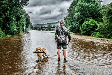 A man and his dog stand on a flooded road. Heavy rain caused the River Lomme to burst its banks resulting in widespread flooding in the provinces of Namur and Luxembourg and Liege.