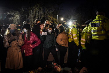 A woman holds up a sign demanding an end to violence again women, as police, citing COVID-19 lockdown regulations, begin to arrest people after attempting to break up a vigil at the bandstand on Claph...