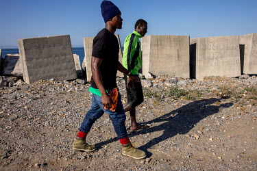 Migrants from Cameroon walking past concrete coastal defences.
