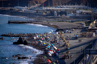 A crowded beach in the Spanish exclave of Ceuta beside the border fence and Morrocan customs facilities.
