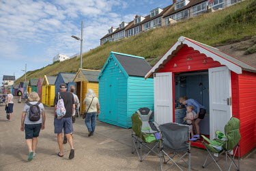Tourists walk past a row of colourful beach huts on the sea front.Sheringham is a Victorian-era English seaside resort that was popular up through the 1950s before mass travel to other parts of Europe...
