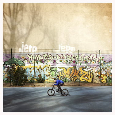 A boy rides a bicycle in a playground surrounded by a graffiti covered wall.  The Berlin district of Moabit is an artificial island completely surrounded by water that was once home to various industr...