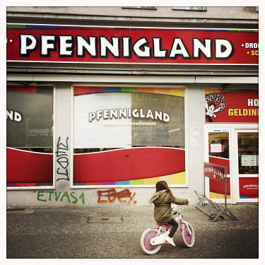 A child rides a bicycle outside the now closed discount shop Pfennigland.  The Berlin district of Moabit is an artificial island completely surrounded by water that was once home to various industries...