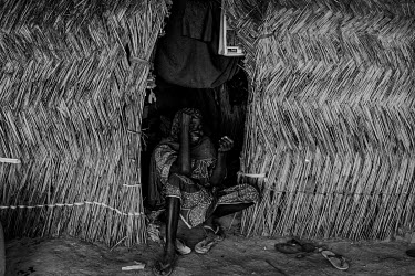 A woman relaxes in the doorway of a thatched shelter in an unofficial camp for displaced people.