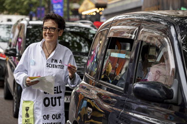An Extinction Rebellion activist wearing a lab coat emblazoned with 'I am a Scientist' talks to drivers during a march and occupation in London's West End.