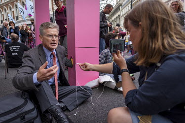 'Nigel', an Extinction Rebellion activist, is filmed and interviewed by a woman using a smartphone while locked on to a structure in St Martin's Lane, part of an occupation protest in London's West En...