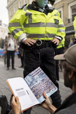 An Extinction Rebellion activist sits in the road, beside a policeman, reading the New Scientist's Essential Guide to Climate Change during a march and occupation in London's West End.