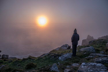 The sun sets into a heavy coastal mist at Land's End, the western most spot on the British mainland.