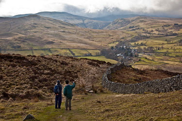 A father and daughter look back towards a village while hillwalking.