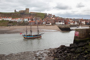 A 3 masted sailing ship enters Whitby Harbour with tourists on board.