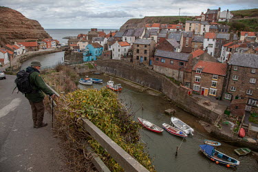 A walker looks down at boats in Staithes harbour, a traditional fishing village on the North Yorkshire coast that attracts coastal walkers and other visitors.