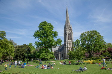 People picnicking in an East London park with a church steeple in the background.