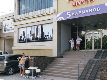 A woman stands next to a table and two stools outside a shopping center in Tiraspol.