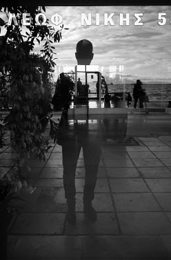 People walking along the promenade are reflected in a shop window.