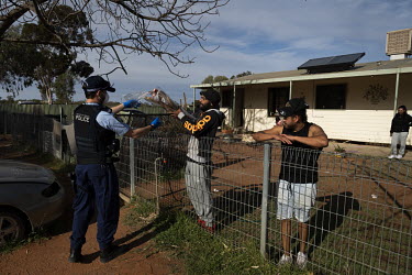 A police officer hands several kangaroo tails, a favourite food for Barkindji Aboriginal people, to Ronnie Murray who is currently isolating with his family in a small house.
