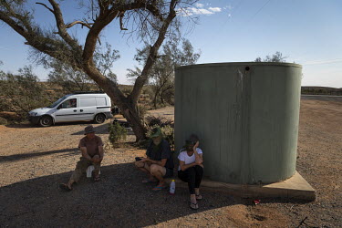 A group of stranded travellers sit under a water tank during the day as temperatures rise. These residents of South Australia are camped out in a roadside truck stop in the middle of the outback, arou...