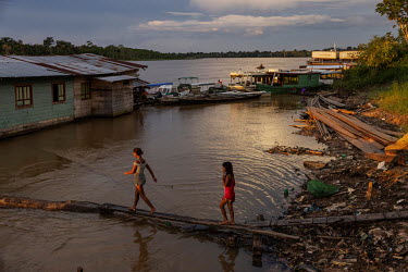 Two girls walk along a wooden plank to reach a hut built on the banks of the Javari river in the Vale do Javari indigenous territory.