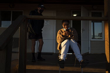 Christine Hunter sits on the deck outside her room with family member Jai Kirby, quarantining from other family members in the temporary Warrawong caravan park quarantine facility.