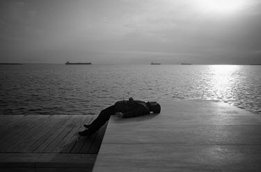 A man lies on a stone surface while smoking a cigarette on the promenade.