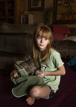 Jade Stephan sits in her family's living room and feeds â��Chari', a rescued wombat from a bushfire that passed through the forest near Braidwood in New South Wales in January. Jade and her mother Do...