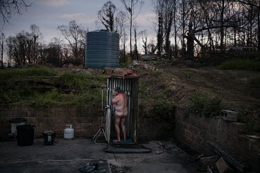 Grant Brown washes in a makeshift shower he has placed on the corner of the concrete slab that used to be the base of his home before bushfires destroyed it.  Grant Brown and Venessa Downing now live...