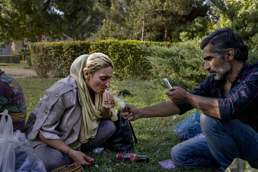 A man lights a methamphetamine pipe for a woman in a city park.