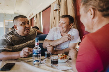 Three men talk and share food and alcohol on a train. In Kazakh on-board restaurants the atmosphere is often exuberant. The wagon is filled with laughter and the smell of borscht. The waitresses bring...