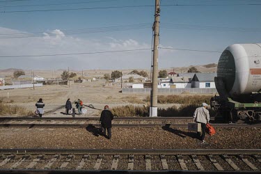 People walk across the train tracks with their luggage after getting off a train.
