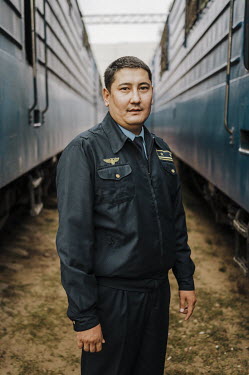 A uniformed train guard stands between trains in the station at Almaty.