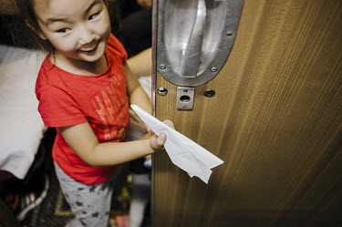 A girl plays with a paper aeroplane on a long distance train journey.