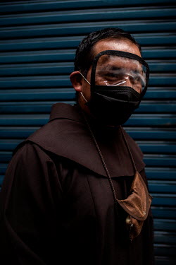 A Franciscan priest poses for a portrait while waiting to be served at a bank in Quito. He's wearing a protective face covering.