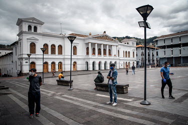 People stand apart, socially distanced, in front of a private clinic on Plaza del Teatro in Quito.