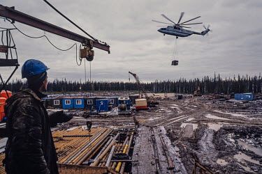 An oil worker looks on as a helicopter delivers crews and equipment for building a basecamp in roadless wilderness near the Arctic Circle as part of an Occidental Petroleum joint venture with the Russ...