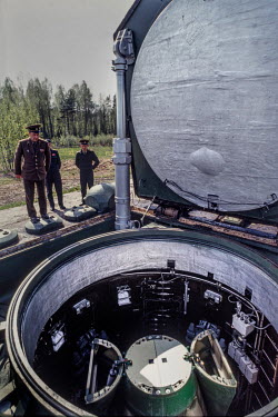Russian nuclear forces officers look down into a silo containing an intercontinental ballistic missile with an exposed rocket head containing four MIRVs underneath.