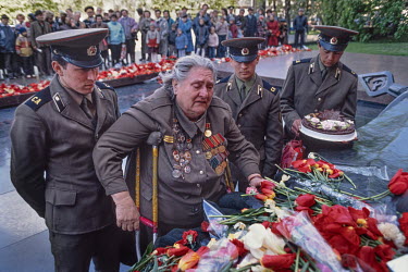 A female veteran of the Great Patriotic War (World War Two) lays flowers at the tomb of the unknown soldier outside the Kremlin, flanked by young soldiers.