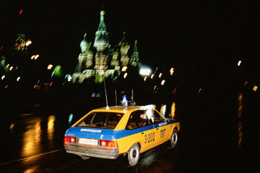 A Moscow militia (police) car speeds past the domes of St Basil's Cathedral at night.