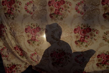 The shadow of a woman sunbathing falls on a floral curtain. The photographer's Grandmother, María Luisa Jaque stayed at home during the Covid-19 pandemic due to her age and diabetes.
