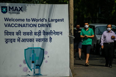 Men in masks walk past the vaccination drive board outside the Max hospital in Delhi.