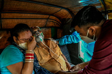 An upset relative holds an older man with Covid 19 who has just lost conciousness. He is receiving free oxygen support in a taxi, while waiting for admission to hospital. The oxygen is provided by vol...