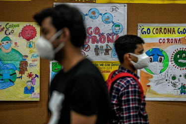 Young men in masks walk past public health posters in the vaccination centre after receiving their first dose of a Covid 19 vaccine at a government school in Delhi. This is phase 3 of the vaccination...