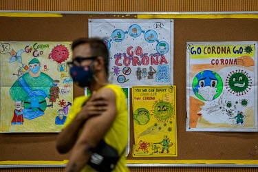 A young man in a mask walks past public health posters in the vaccination centre after receiving their first dose of a Covid 19 vaccine at a government school in Delhi. This is phase 3 of the vaccinat...