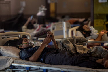 A young man with Covid 19 looks at his phone while receiving oxygen at a temporary facility opposite the Lok Nayak Jai Prakash Narayan hospital in Delhi.