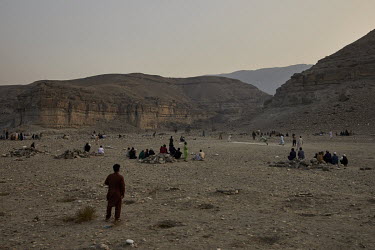 A group of men play a cricket match in the foothills of the Hindu Kush, near Jalalabad, with others looking on.