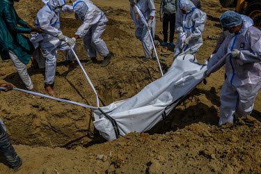 People in personal protective equipment lower the body of a man who died from coronavirus into his grave, during a funeral at a graveyard in New Delhi, India.