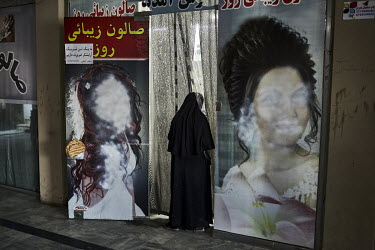 A woman walks into what was once a beauty salon, past advertising that previously showed women's faces that have now been painted over in accordance with strict modesty laws imposed by the new Taliban...