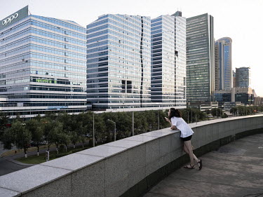 A woman with a mobile phone leans on a wall overlooking highrise buildings along Nurzhol Boulevard.