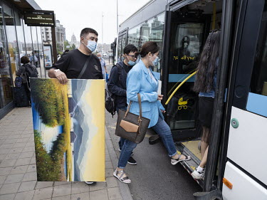 A man carries a painting of an idyllic landscape onto a bus in central Nur-Sultan.
