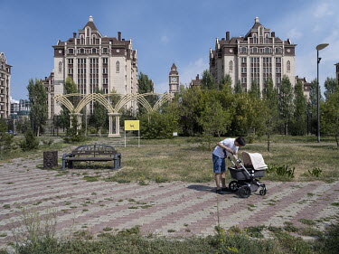 A man tends to a child in a pram in front of newly built luxury condominium complexes in the English Quarter at Panfilov Street.