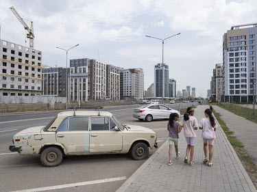 Three girls walk past an old Soviet car on a parking lot in the eastern outskirts of the city.